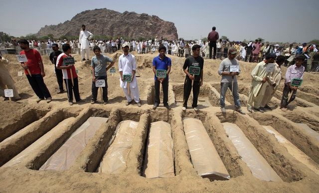 Members of the Ahmadi Muslim community hold the names of victims as they stood over their graves in Chenab Nagar, located in Punjab's Chiniot District